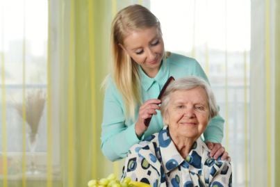 anziana disabile pettinata da caregiver che la assiste
