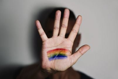 uomo con mano davanti volto con bandiera arcobaleno